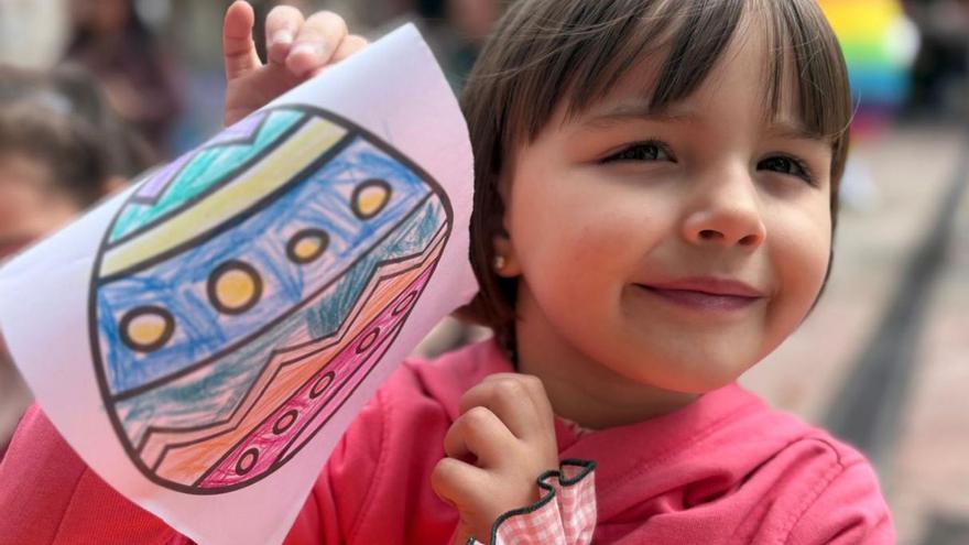 Arriba, una de las niñas participantes enseña su dibujo de un huevo de pascua. Abajo, un grupo de escolaresjunto a dos huevos de Pascua gigantes. | D. O.