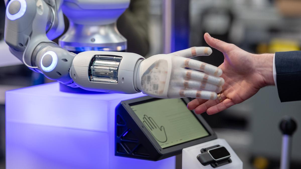 Un robot estrecha la mano a un asistente a una feria tecnológica.
