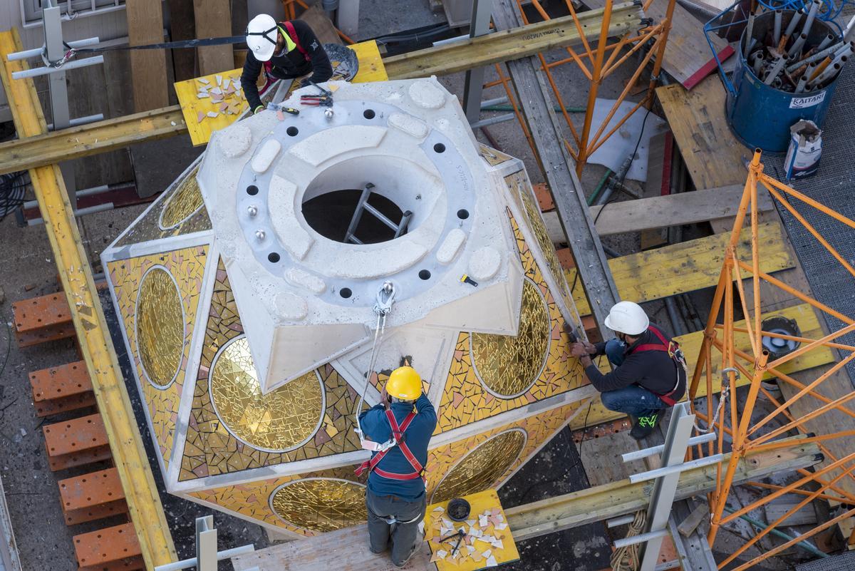 Icosaedro de la base de la escultura del Evangelista Lluc. Colocación del ’trencadís’ en la plataforma de trabajo situada a 54 metros en la cubierta de la nave. Los colores utilizados para ornamentar esta pieza son Oro Orsoni para los casquetes esféricos, y ocre, amarillo y salmón en tonalidades cálidas para las caras de la pieza.