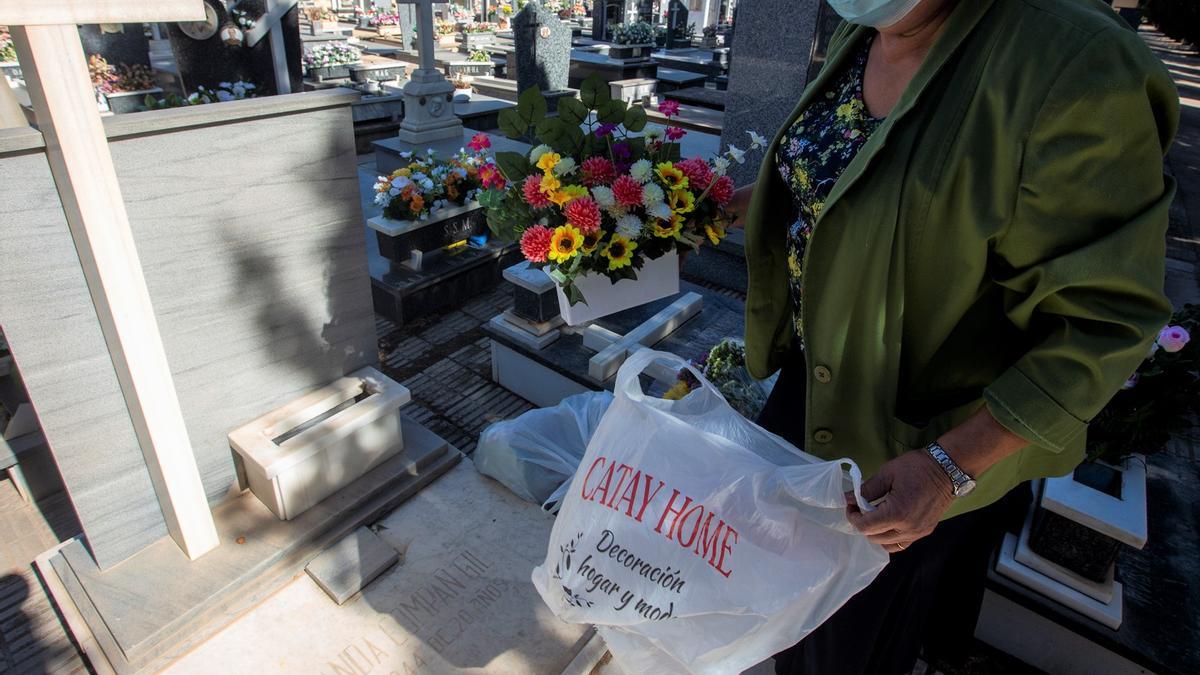 Una mujer, con una maceta de flores artificiales en el Cementerio.