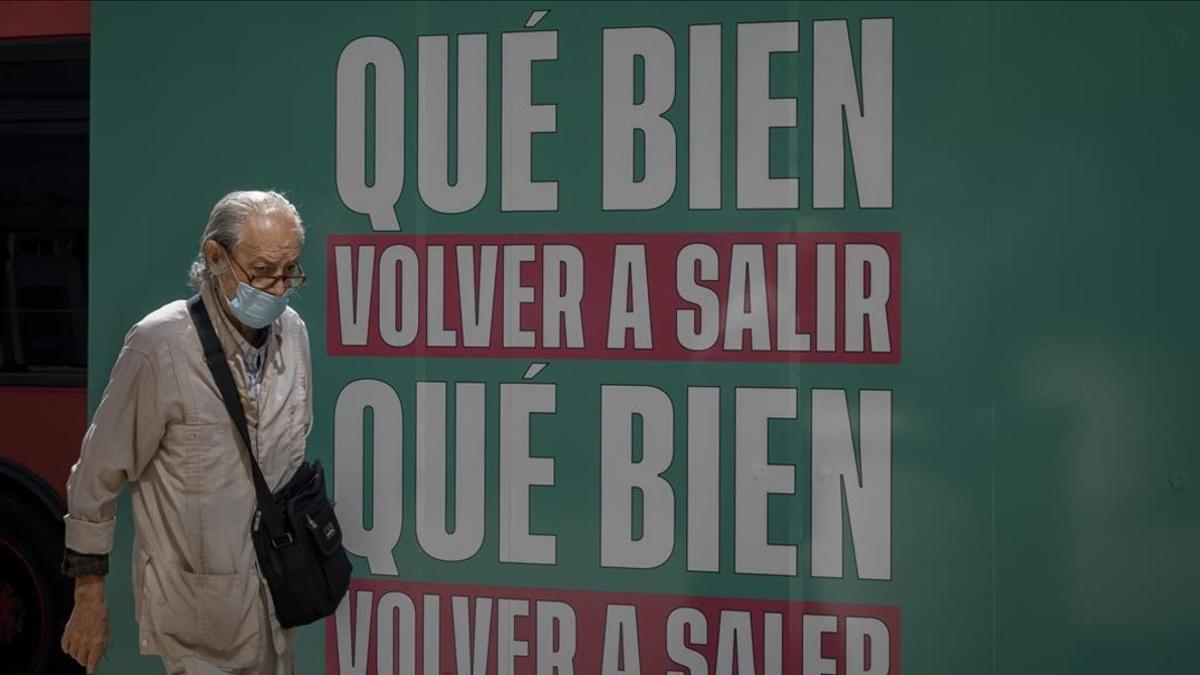 Uh hombre pasea por València tras un cartel que celebra la nueva normalidad