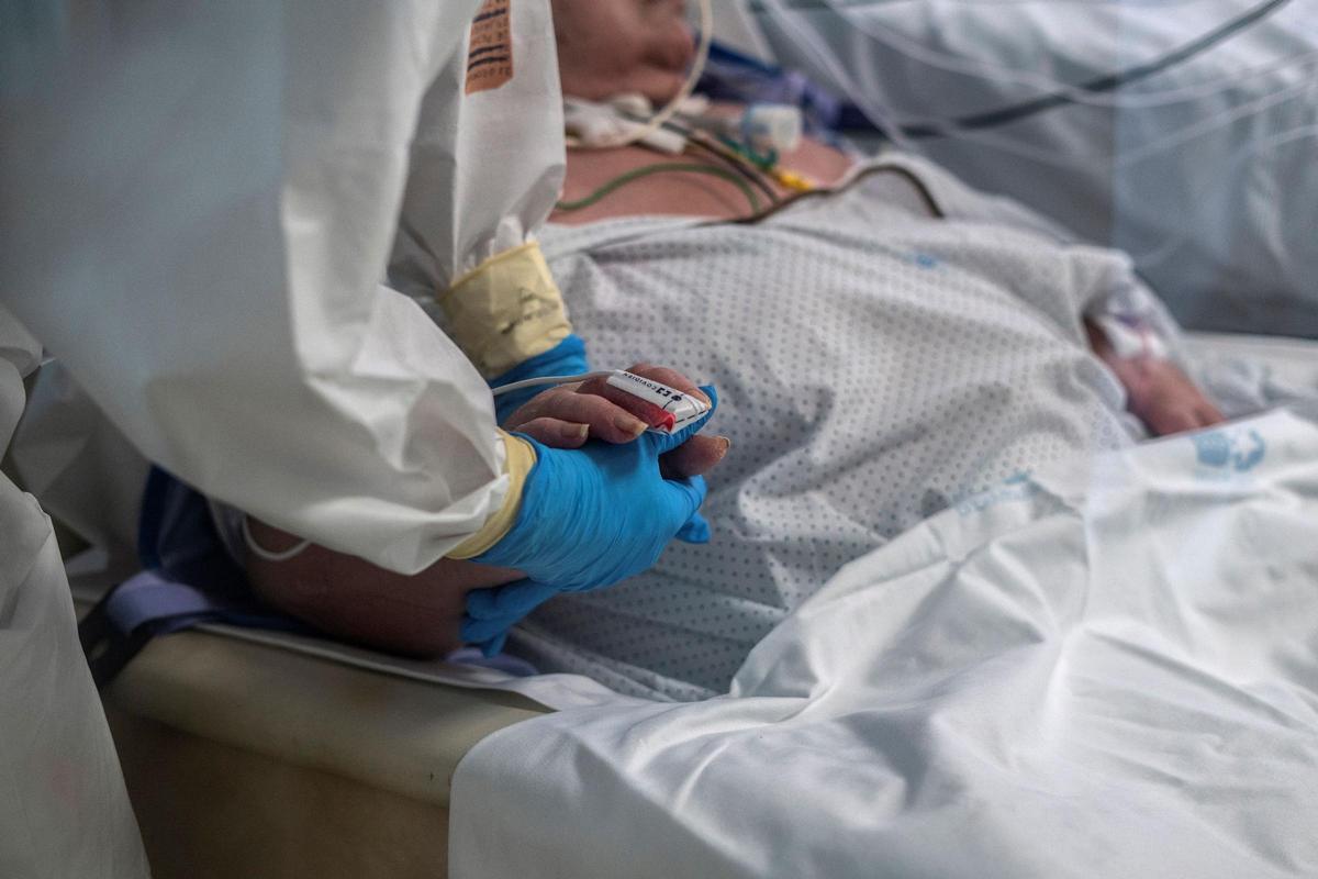 Un sanitario de La Princesa da la mano a una paciente en la pandemia
