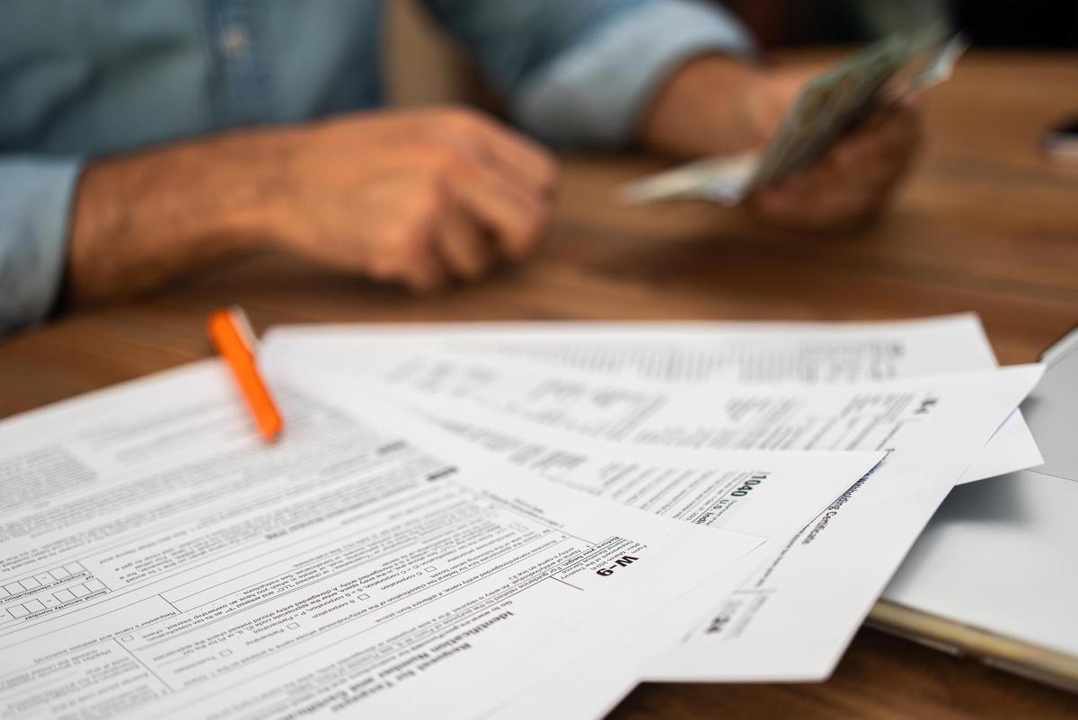 Un hombre sostiene billetes en la mano pensando en los servicios de asistencia profesional para llenar los formularios de impuestos