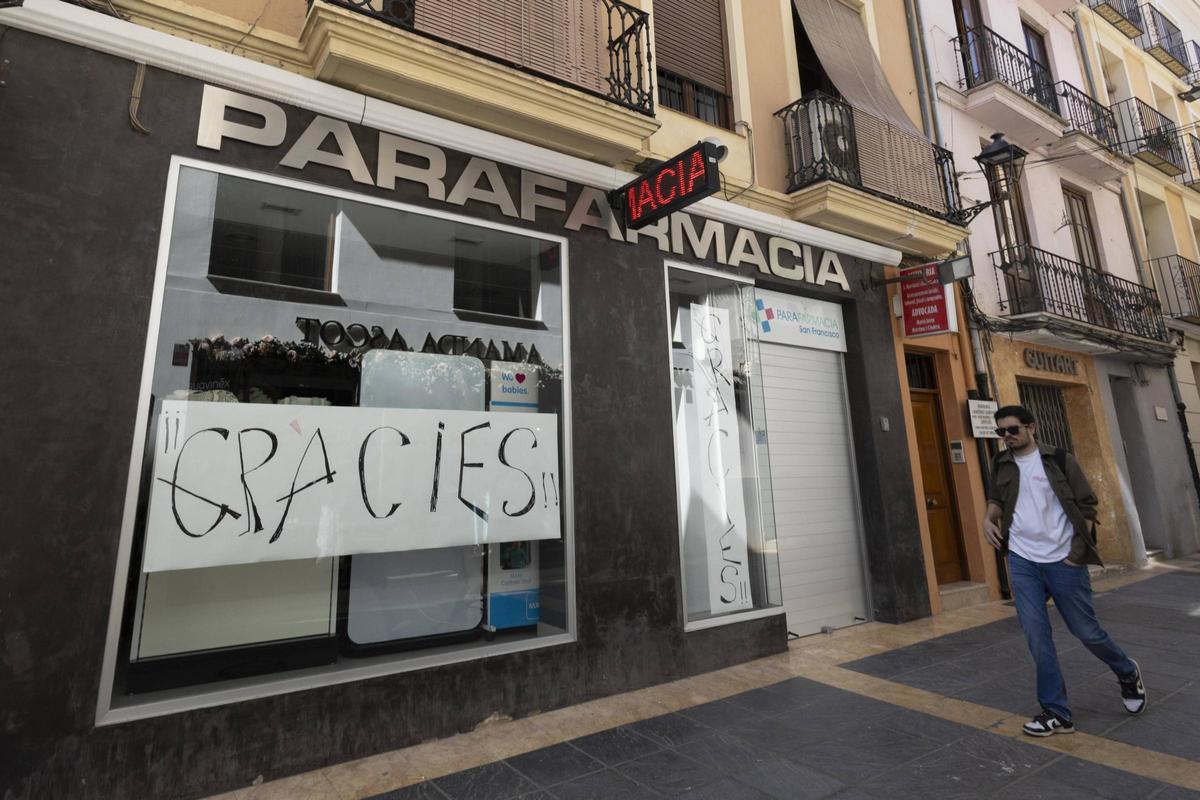 Un hombre pasa frente a la fachada de la parafarmacia de Sant Francesc, que ha bajado la persiana en Xàtiva.