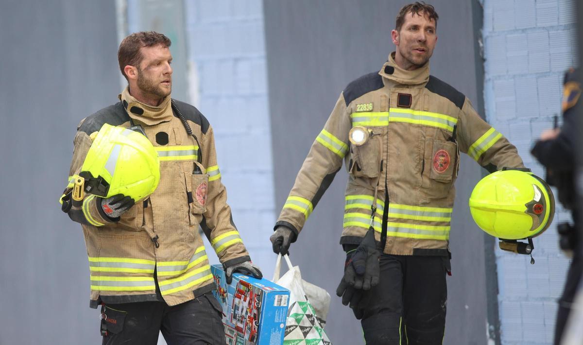 Dos bomberos con algunos enseres de un vecino, tras salir del edificio calcinado.