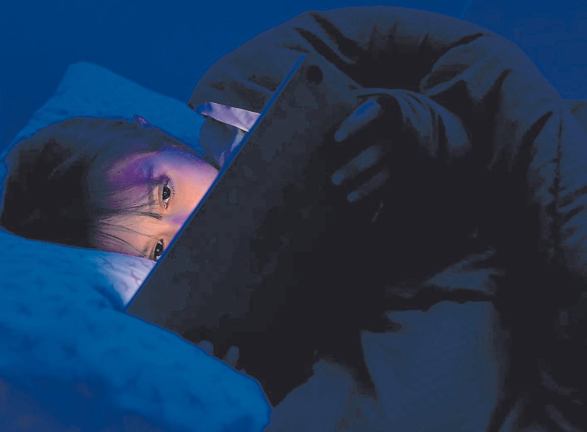 Una menor de edad sujeta una tablet en la cama.