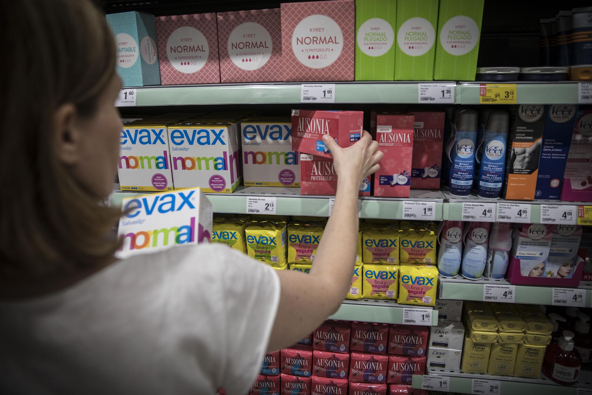 Una mujer elige ante un estante con productos de higiene femenina.