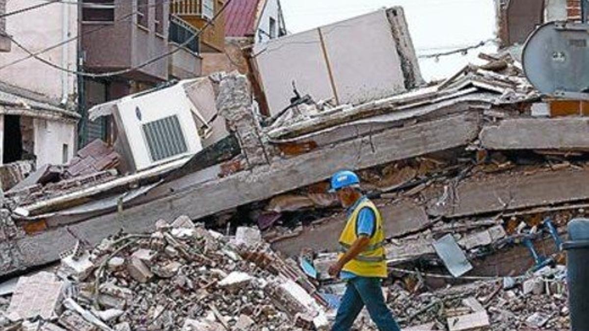 Un miembro de los cuerpos de emergencia camina ante las ruinas.