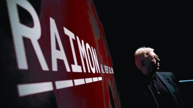 Raimon posa junto al cartel de la exposición 'Raimon. Al vent del món', que recorre su trayectoria desde el primer concierto que realizó en Barcelona.