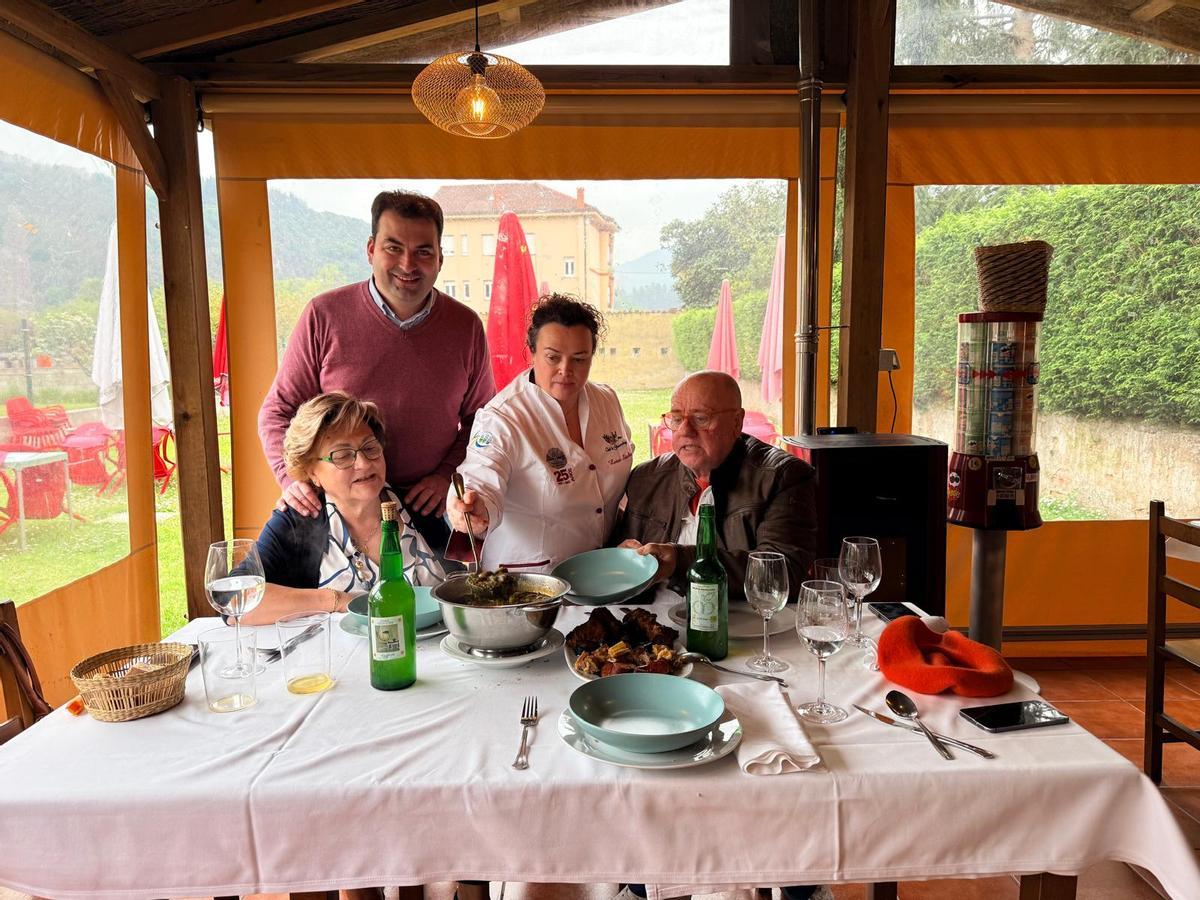 En el centro, la cocinera Luisa Sánchez sirve un plato de pote de castañas a Amada Álvarez y a Carlos M. Guardado, con el alcalde de Salas, Sergio Hidalgo, de pie.