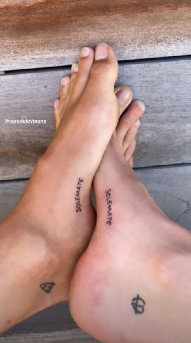 Primer plano de los pies de Kaia Gerber y Cara Delevingne con el mismo tatuaje, la palabra 'solemate'