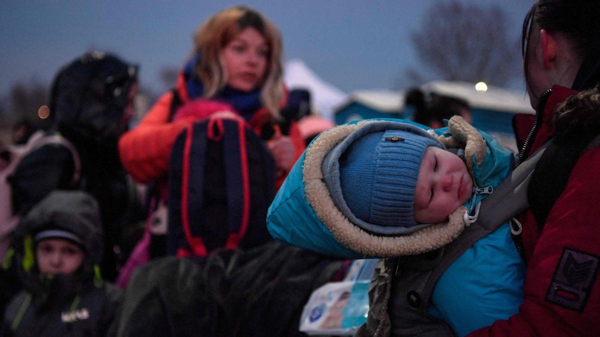 A child is carried by a woman as refugees from Ukraine proceed to a gathering point after crossing the Ukrainian border with Poland at the Medyka border crossing, southeastern Poland, on March 11, 2022. - More than two and a half million people have fled the &quot;senseless war&quot; in Ukraine, the UN said on March 11 -- more than half to Poland. (Photo by Louisa GOULIAMAKI / AFP)