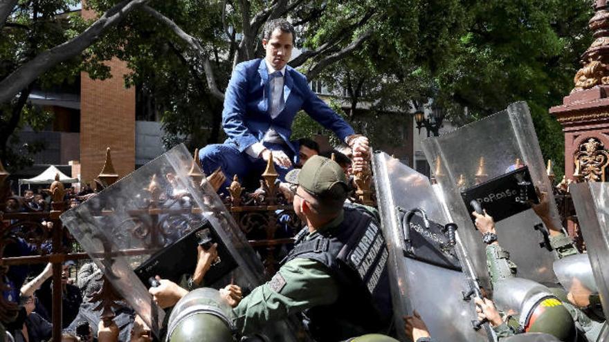 Juan Guaidó intenta salta la verja exterior para acceder al Parlamento mientras se lo impide la Guardia Nacional.