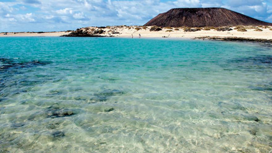 Vista panorámica de Lobos, con dos bañistas en una de sus playas de aguas cristalinas y su montaña que se erige al fondo.