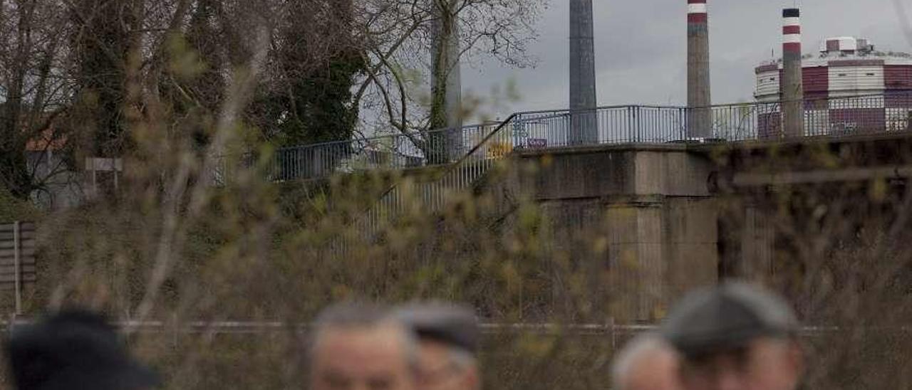 Varios vecinos dan un paseo por Llaranes, con las chimeneas de las baterías de coque al fondo.