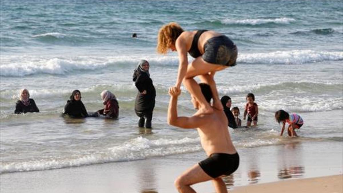 Tel Aviv 8 Varias mujeres se bañan vestidas y contemplan las acrobacias de una pareja en 'shorts' y bañador.