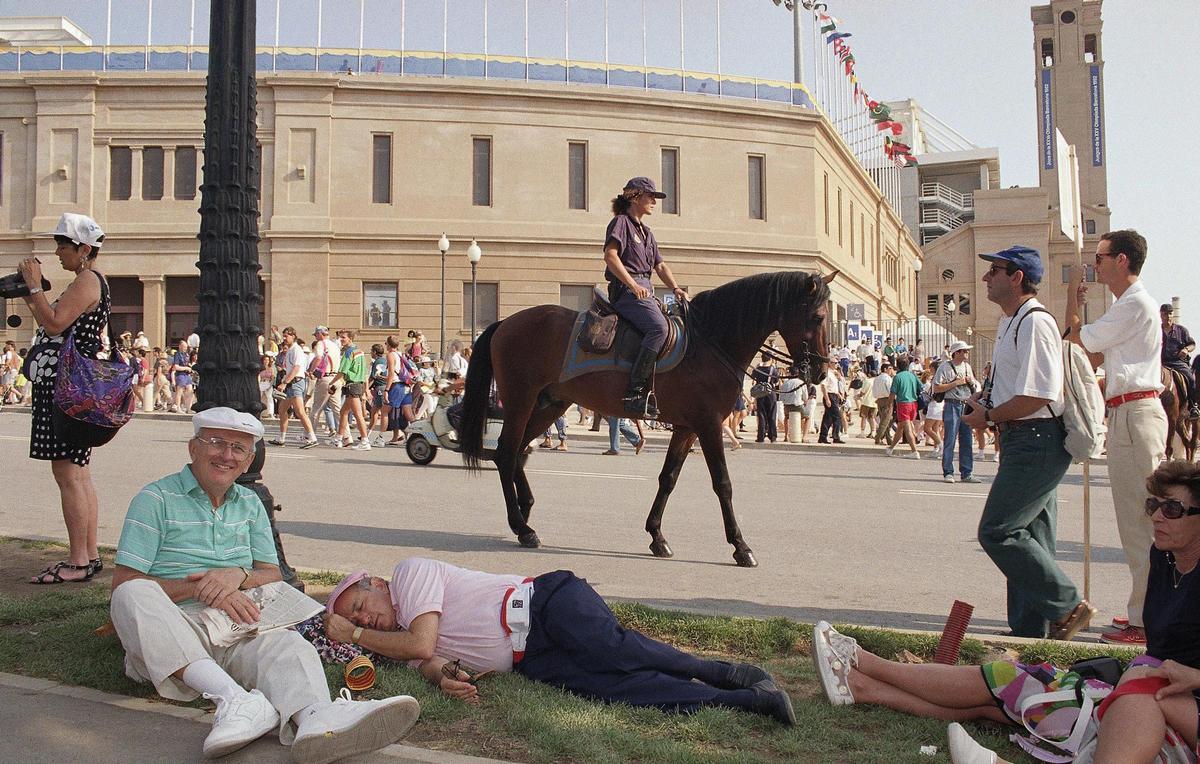 Un hombre duerme en la hierba y otros descansan, frente al Estadio Olímpico de Barcelona, mientras pasa un policía montado a caballo. La escena se capta poco antes de la ceremonia de inauguración de los Juegos Olímpicos de Barcelona, el sábado 25 de julio de 1992.