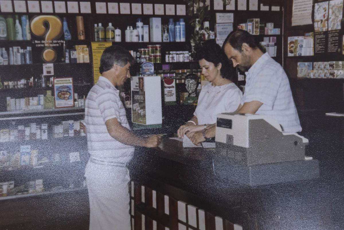 Gustavo Rodríguez antendiendo a una cliente tras el mostrador de su farmacia en la década de los 80.