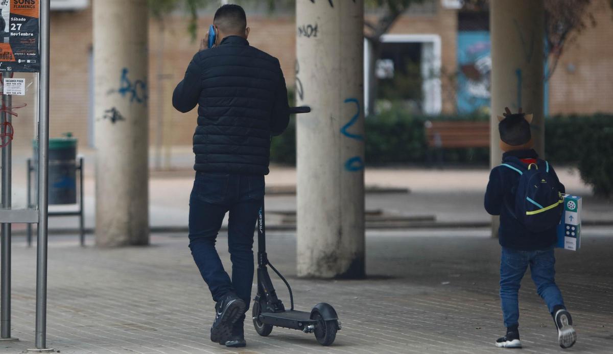 Un usuario de patinete lo arrastra sobre la acera de una avenida del Port de Sagunt.