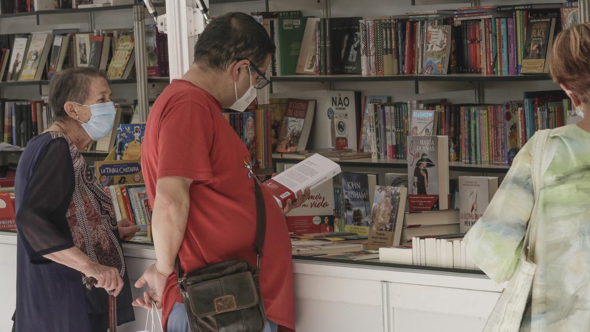 Un cacereño ojea un libro en un expositor de la feria del libro.