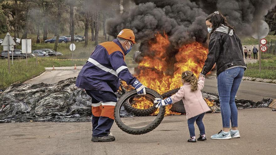 Un trabajador de Alcoa acerca un neumático a una barricada en compañía de una niña y de una joven, ayer, durante las protestas en San Cibrao.