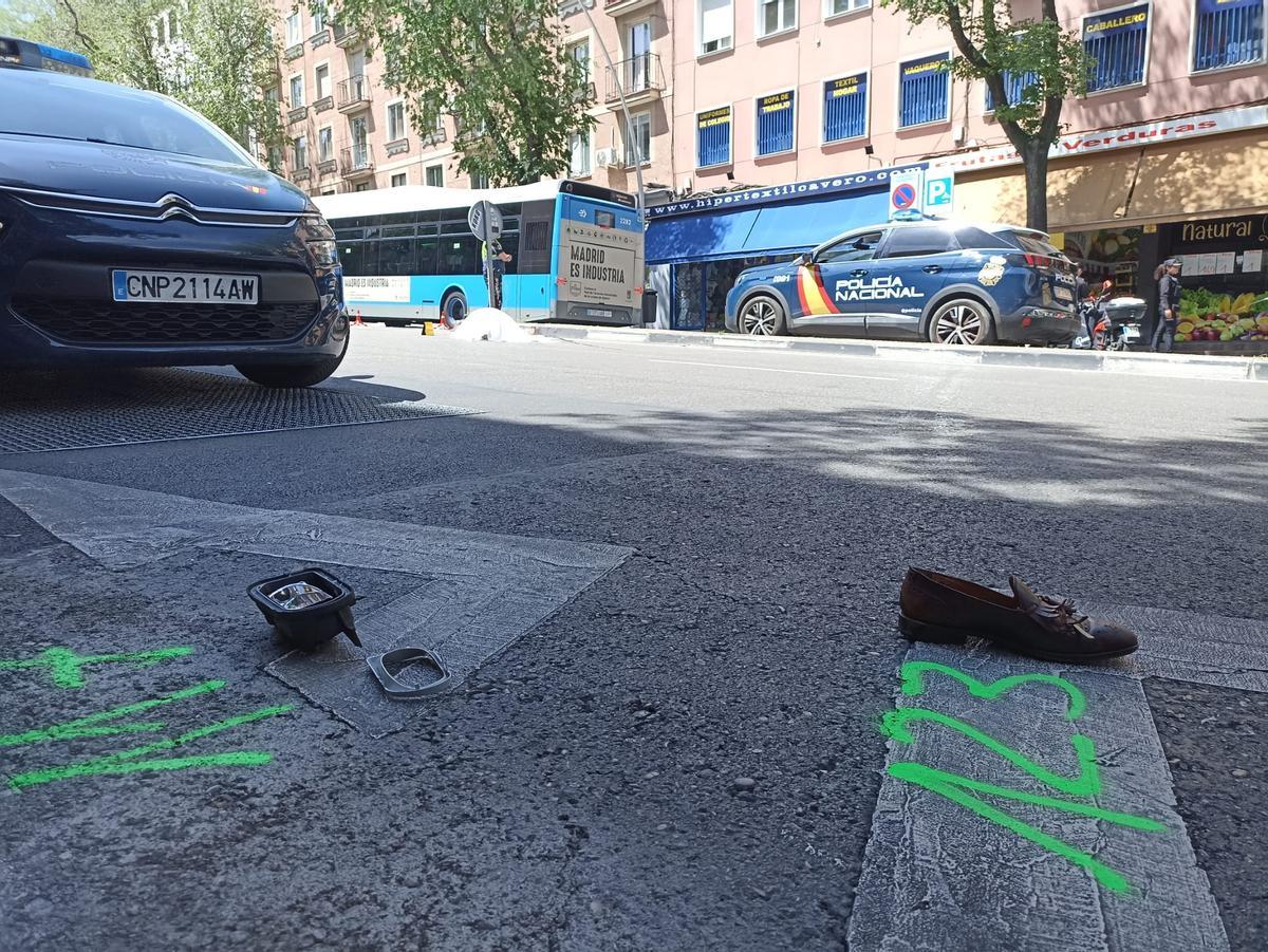 El cadáver de una de las personas atropelladas en el Paseo de Extremadura, al fondo; en primer plano, un objeto personal del fallecido y el retrovisor del coche
