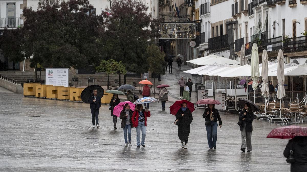 Varias personas con paraguas bajo la lluvia en la plaza Mayor de Cáceres.