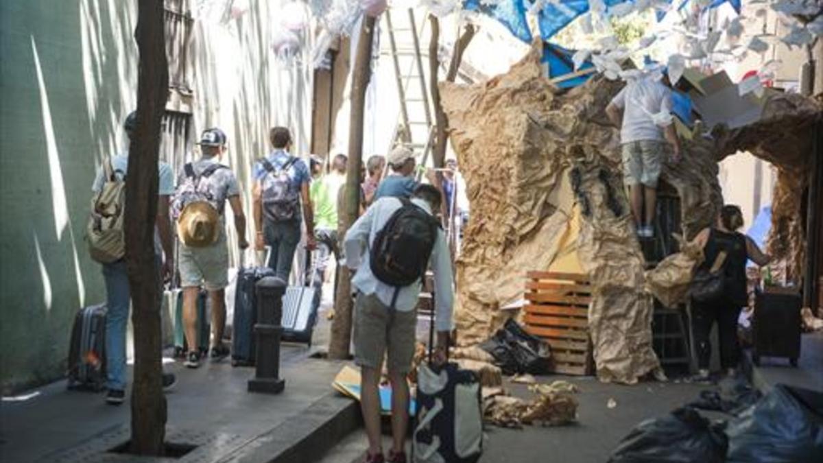 Turistas con su equipaje entre los vecinos engalanando una calle de Gràcia.