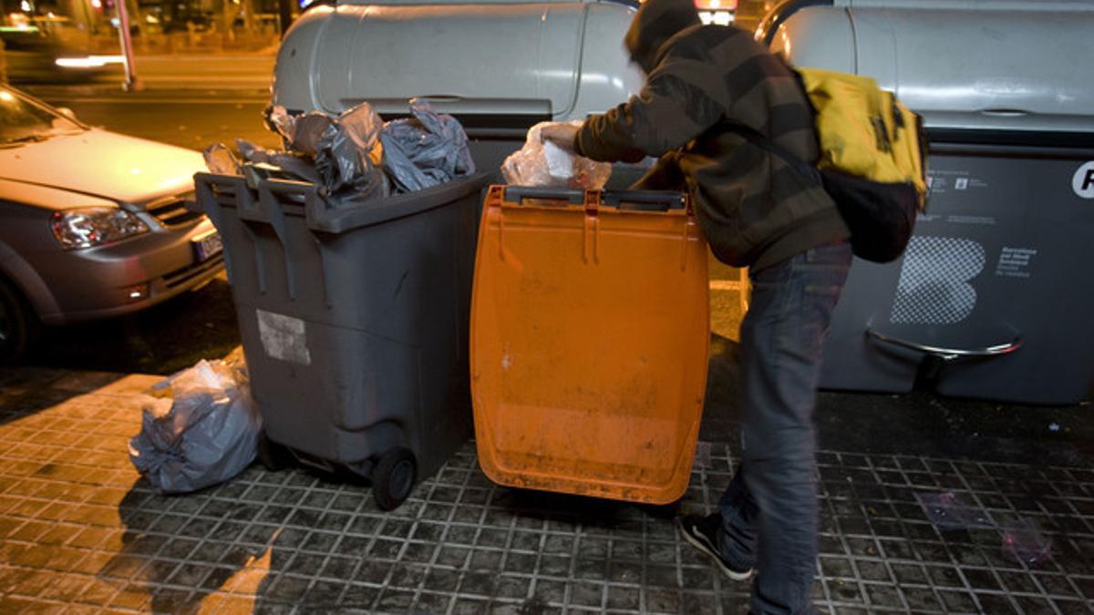 Un joven busca comida en un contenedor de basura orgánica, en Barcelona.