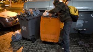 Un joven busca comida en un contenedor de basura orgánica, en Barcelona.