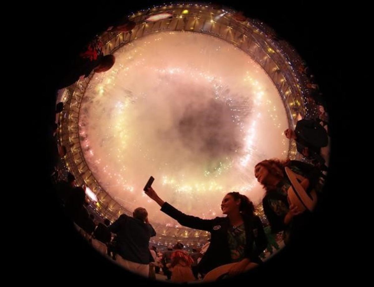 Unos espectadores hacen fotos de los fuegos artificiales durante la ceremonia de inauguración