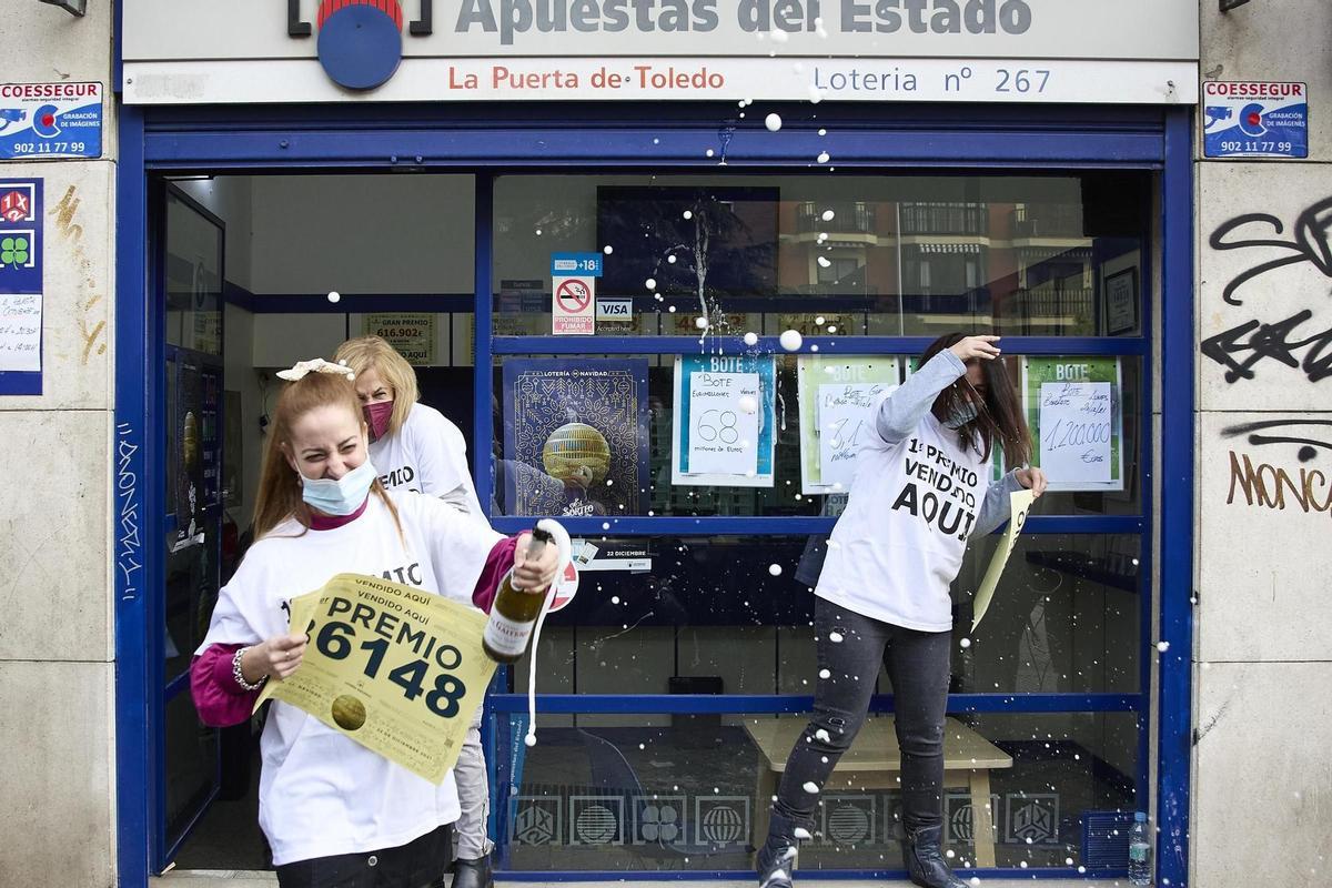 Unas premiadas descorchando una botella frente a una administración