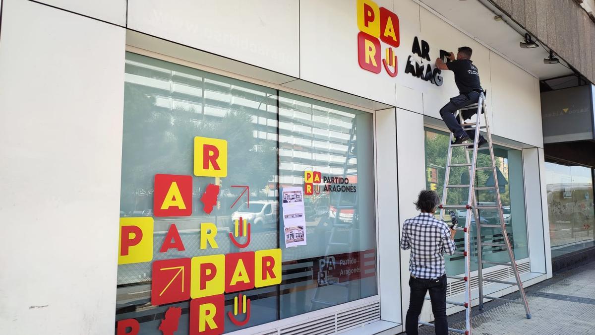 Dos operarios instalan las nuevas siglas del PAR en su sede de la calle Tarragona de Zaragoza.