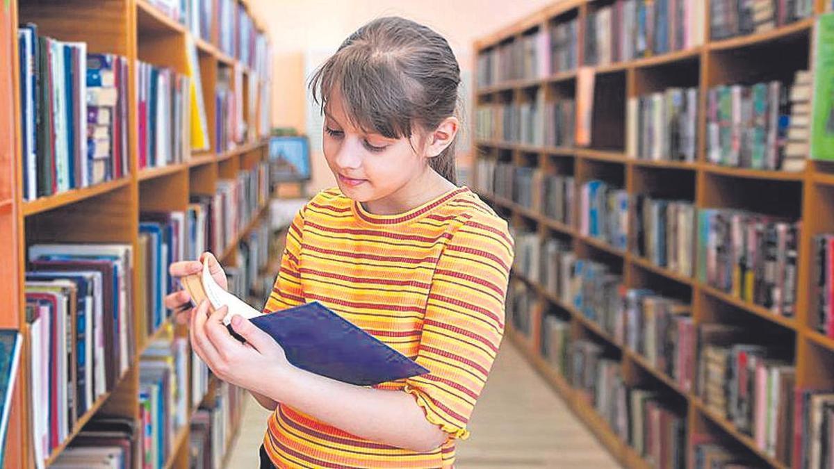 Una niña hojea un libro en una biblioteca.