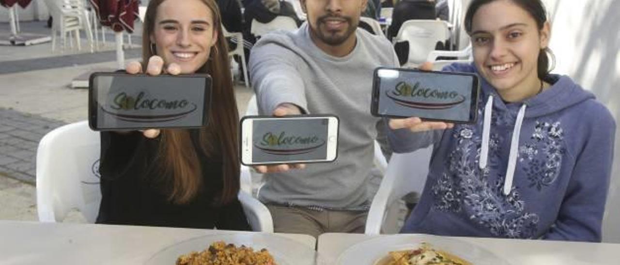 Claudia Cambra, Juan Ortiz y Yaiza Panizo muestran la app «Silocomo» frente a un plato de arroz y otro de pescado.