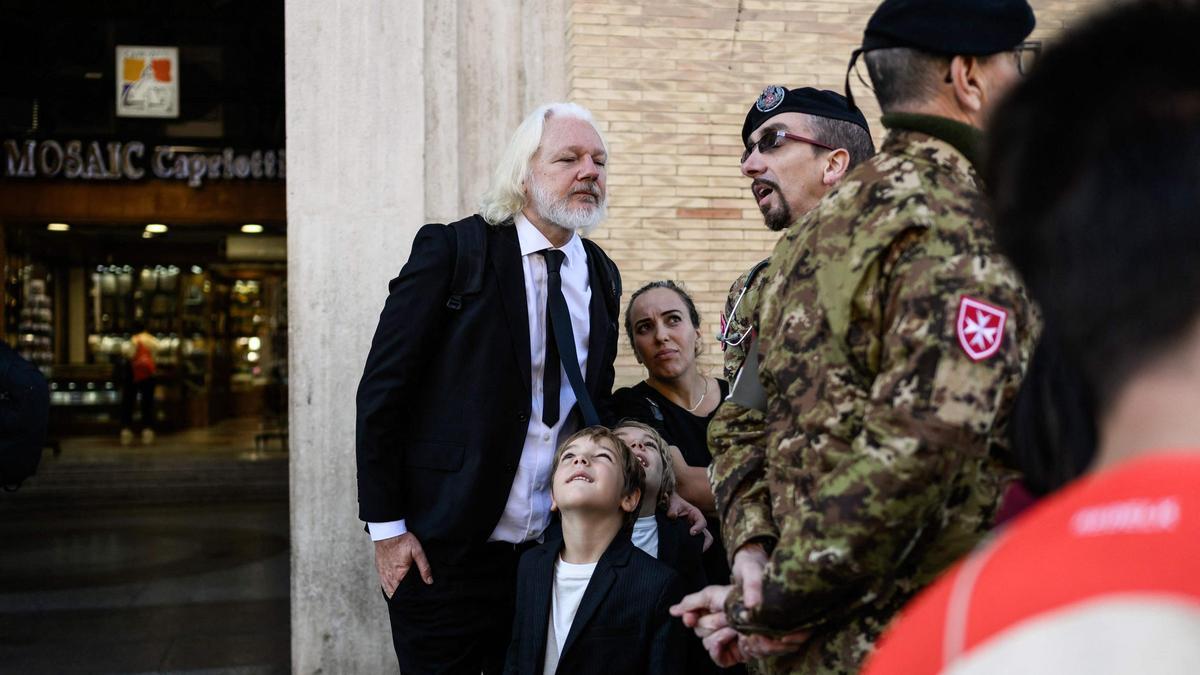 El fundador de WikiLeaks, Julian Assange (izquierda), conversa con un miembro de las fuerzas militares en la Vía de la Conciliazione, junto a la Plaza de San Pedro en el Vaticano, el 26 de abril de 2025, durante la ceremonia funeral del fallecido papa Francisco.
