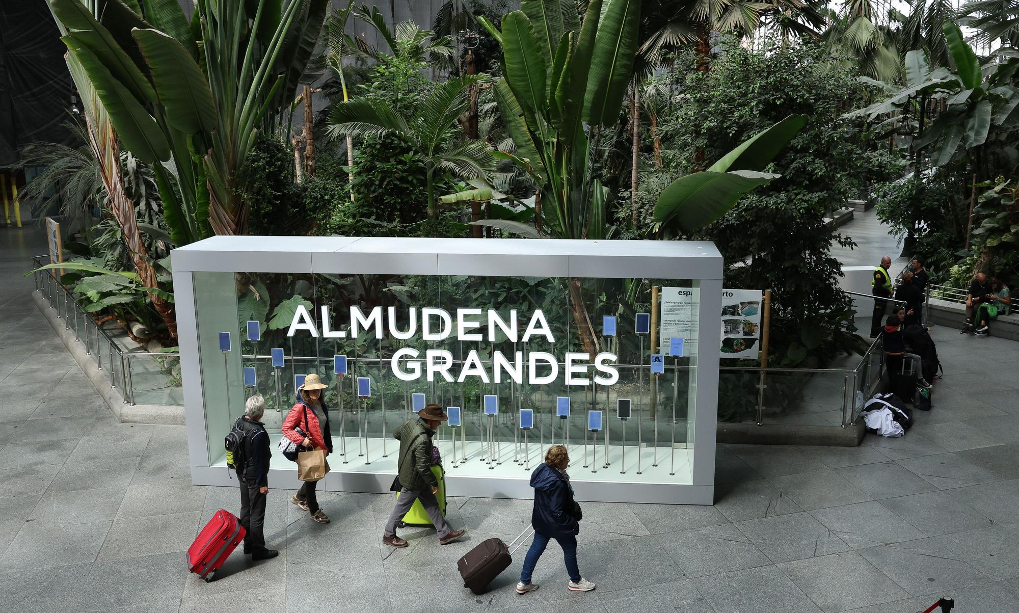 Varias personas caminan frente a la placa de la nueva denominación de la estación Madrid Puerta de Atocha Almudena Grandes.