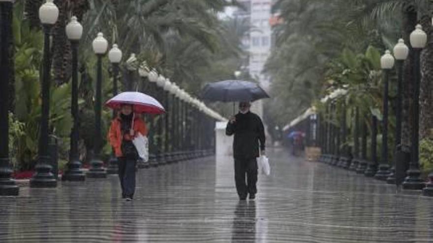 Dos personas caminan bajo la lluvia por el paseo de la Explanada de Alicante.