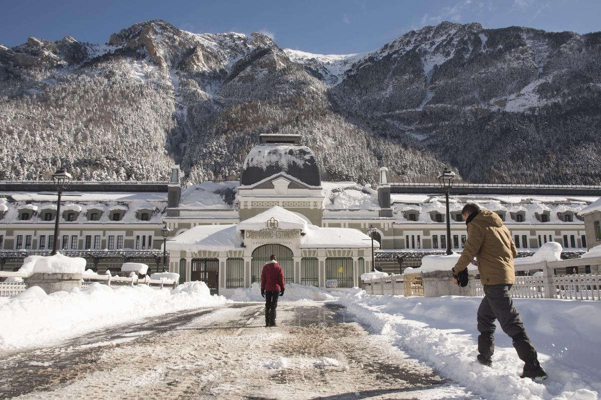 HUESCA, 18/01/2023.- Varias personas pasan delante del edificio de la antigua estación de tren de Canfranc, cubierta por la nieve acumulada. El primer gran temporal del invierno en España, por el paso de la borrasca Fien, ha cubierto hoy de nieve la mitad norte peninsular, lo que dificulta el tráfico en más de un centenar de carreteras, especialmente el de camiones, varias vías se han visto afectadas por inundaciones y se han suspendido rutas escolares en varias comunidades. EFE/ Javier Blasco