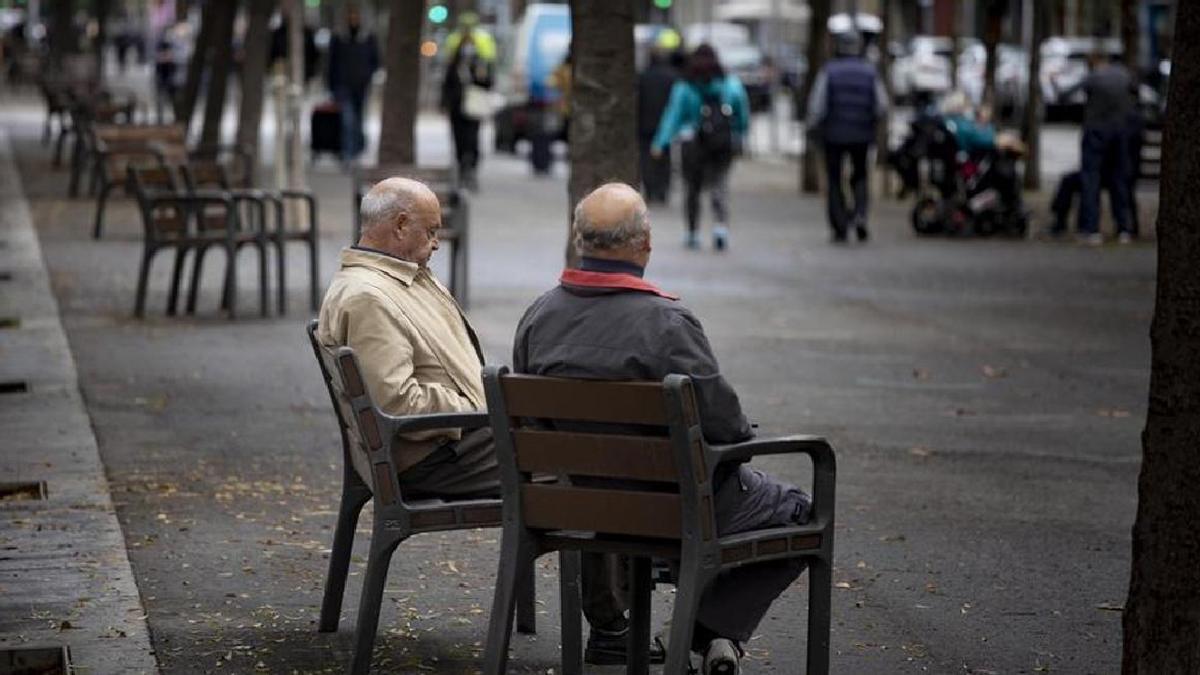 Dos pensionistas conversan mientras descansan en un banco.