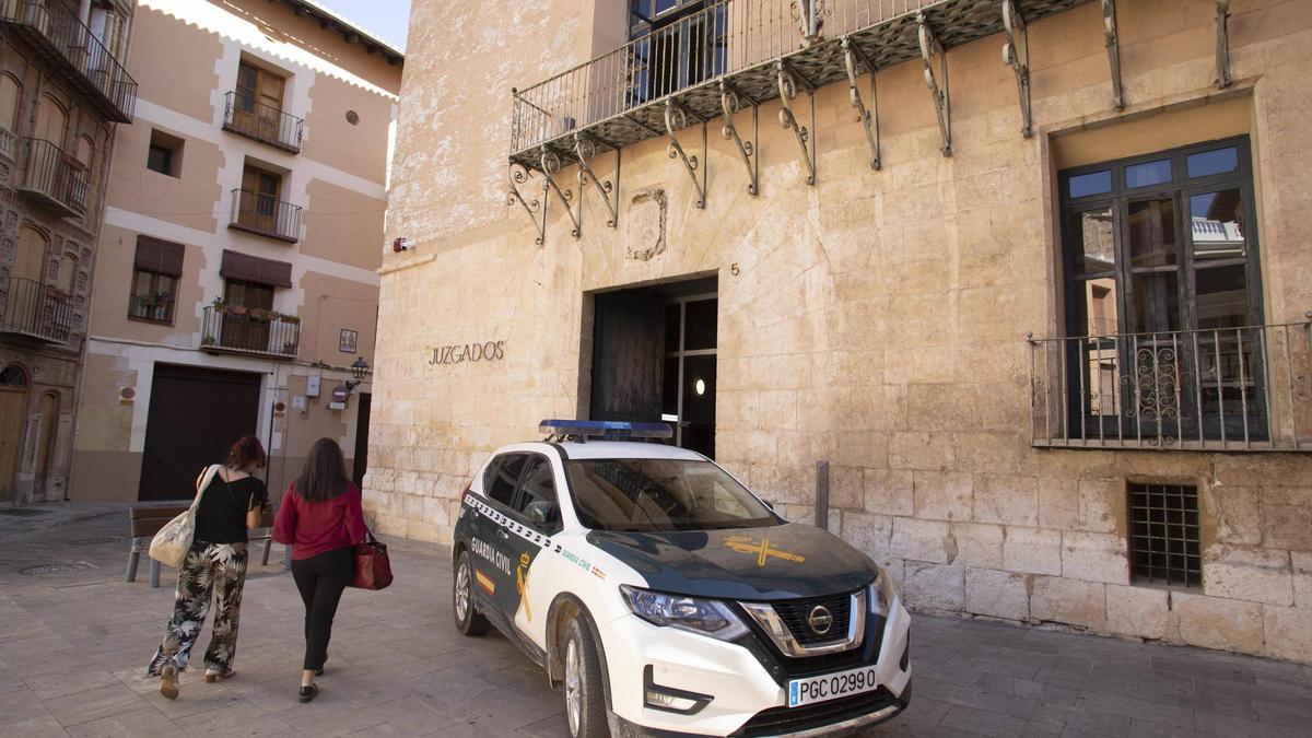 Dos mujeres pasan por delante de un coche de la Guardia Civil en la puerta de los juzgados de Xàtiva.