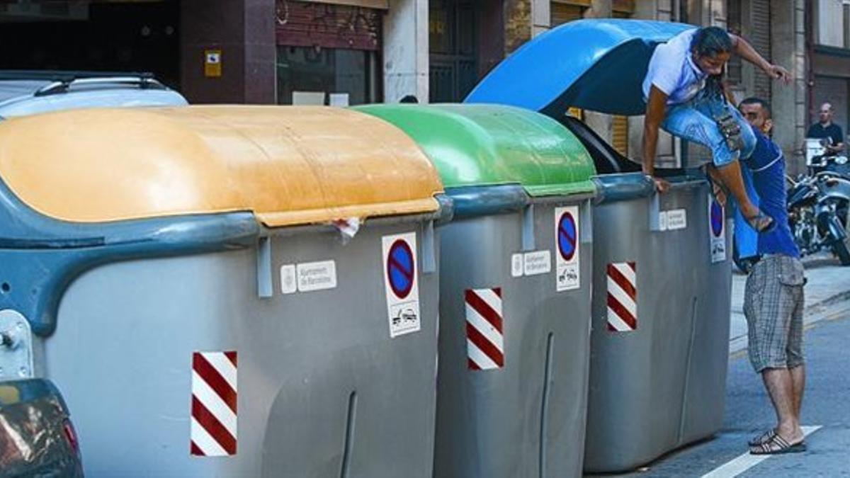 Una pareja busca cartón y papel en un contenedor azul, en la calle de Ausiàs Marc, en septiembre.