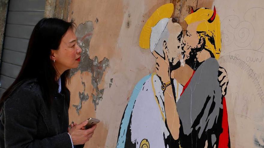 Una mujer observa en Roma un mural que representa a un diabólico Trump besando en los labios al Papa.