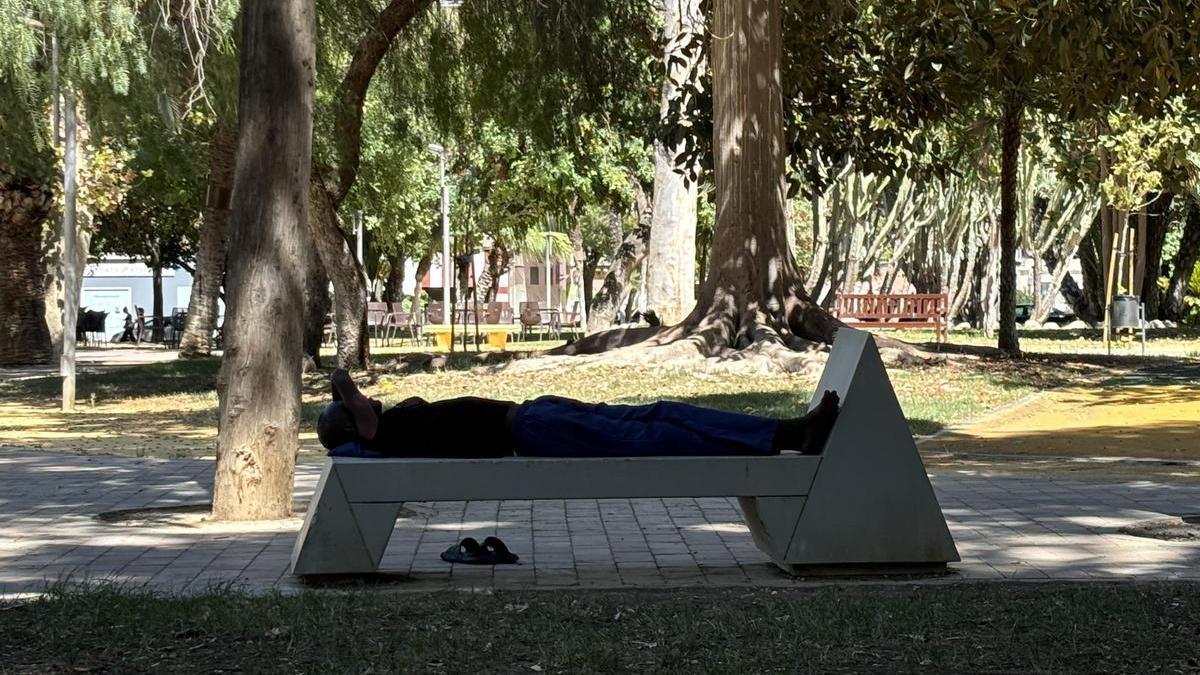Un hombre sin techo descansa en un banco a la sombra del Parque de La Pólvora de Murcia.