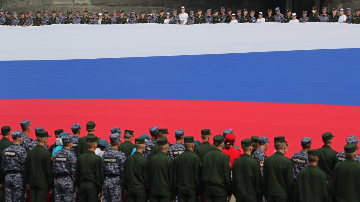 Soldados rusos sostienen una gigantesca bandera, durante el Día de la Bandera Nacional, este lunes.