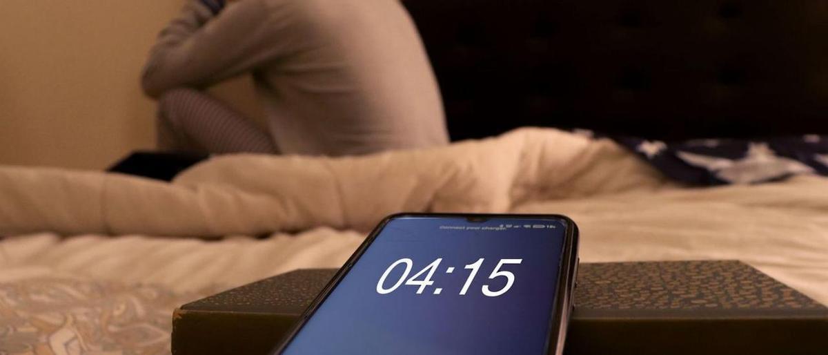Una persona, incapaz de dormir junto a un móvil que marca las cuatro y cuarto de la madrugada.