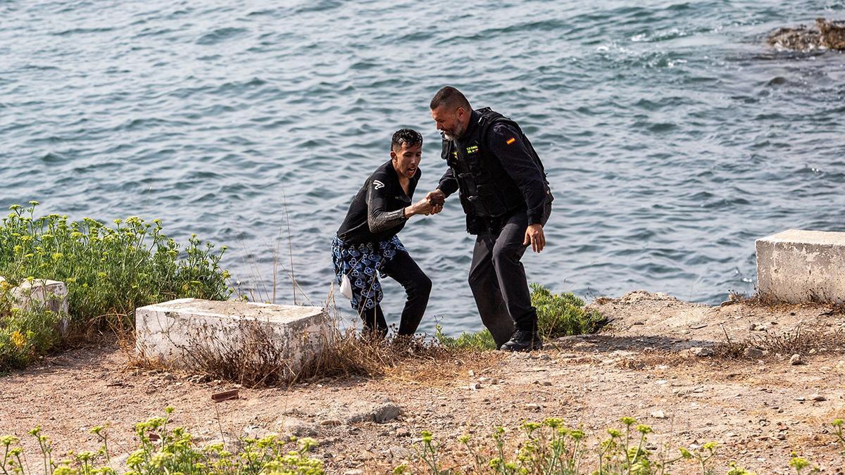 Un miembro de los equipos de rescate españoles asiste a un migrante a su llegada a nado a Ceuta.