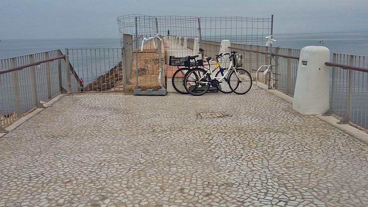 Dos bicicletas aparcadas sobre la valla sujetada con cadenas y cables que cortan el acceso al segundo tramo del paseo de l’Escollera.