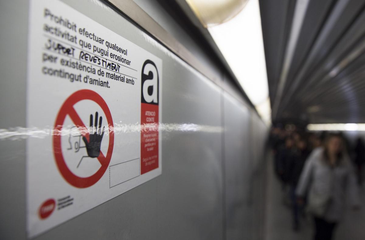 Un cartel avisa de la presencia de amianto tras el revestimiento de las paredes del pasillo de enlace en la estación de metro de Catalunya, en una imagen de archivo.