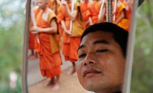 Un conductor cambodjà s’afaita mentre uns monjos budistes passen en una marxa per la muntanya d’Udon durant la cerimònia del Dia de Vesak, per celebrar el naixement i la mort de Buda.